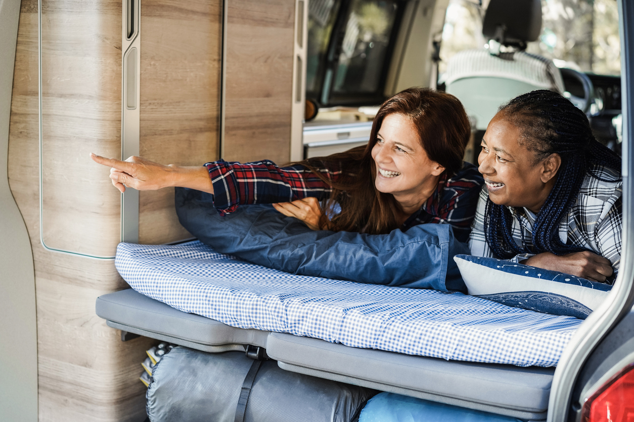 Multiracial women friends having fun camping inside tent/camper van while lying on rv mattress